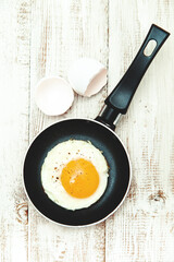 Fried egg in a frying pan on a wooden background.