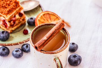 A cup of coffee with cinnamon, fresh berries, sliced orange and a piece of berry cake on white table. Coffee and berry dessert