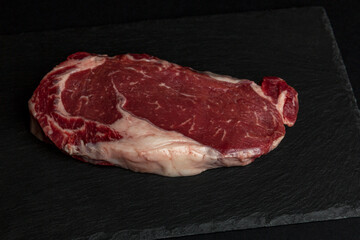 Raw marbled beef ribeye steak on a black stone board. Healthy food. Close-up.