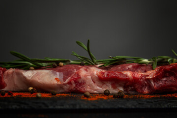 Raw ribeye steak with rosemary and seasonings on a black stone board. Healthy food. Close-up. Profile view. Space for text.