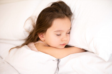 Obraz na płótnie Canvas A cute pretty little girl sleeps on a white pillow. Morning. Bedroom. Lifestyle.