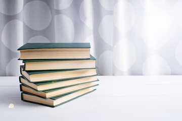 A stack of six green-covered books lying on a white table on the left.