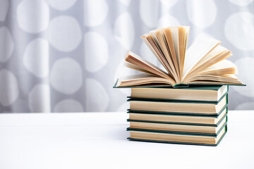 A stack of books and an open book lying on a white table.