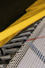 Selective focus on powerful steel springs in the design of the trampoline under the yellow mat.