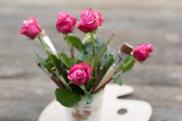 Rosen und Pinsel in einer Vase auf einer Malerpalette
