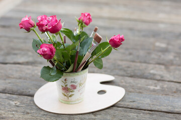 Rosen und Pinsel in einer Vase auf einer Malerpalette