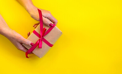 Woman hands holding gift, yellow background.