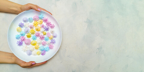 Top view of hands wich holds plate with delicious colorful meringue cookies. Sweet decor. 