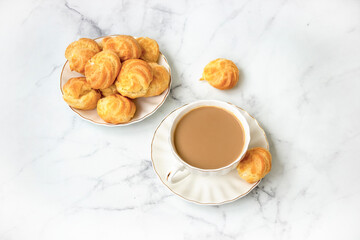 Homemade profiteroles stuffed with whipped cream and milk tea. On a marble light background. View from above.