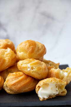 Homemade profiteroles stuffed with whipped cream On marble light background.