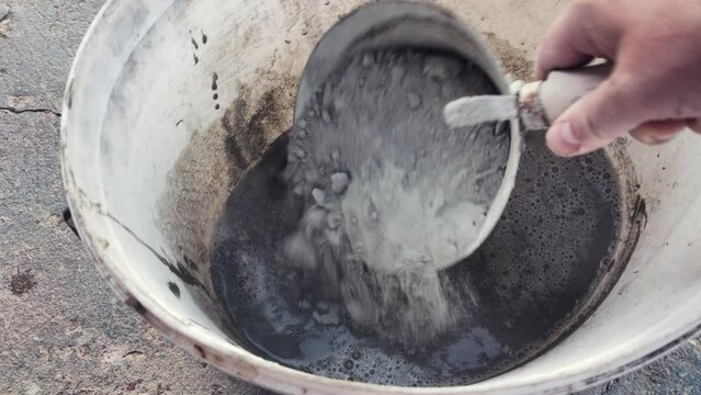 A construction worker pouring cement into the white bucket with water. Point of view shot