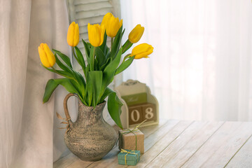 Bouquet of tulips on a white table. In the background is the interior of a white kitchen and a window. The concept of home comfort. The concept of International Women's Day on March 8. Spring flowers.