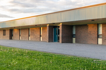 School building exterior and schoolyard with green grass in front on a sunny evening. Elementary public school entrance.