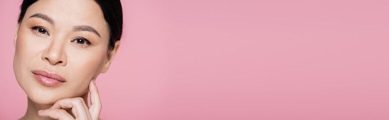 Obraz premium Asian woman with makeup looking at camera isolated on pink, banner