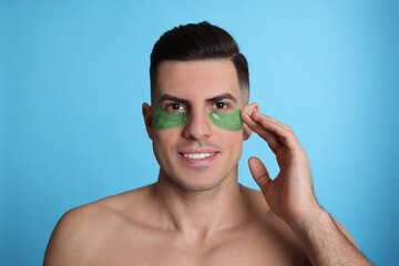Man applying green under eye patch on light blue background