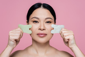 Asian woman holding jade stones near cheeks isolated on pink