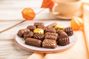 Chocolate candies with cup of coffee and physalis flowers on a white wooden background. side view, selective focus.