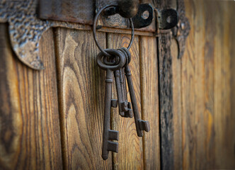 A bunch of old iron keys hanging on a deadbolt on a wooden door