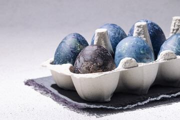 Blue easter eggs dyed with hibiscus tea in an egg carton on a white concrete background
