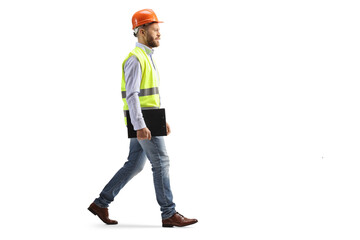 Full length profile shot of an engineer with a hardhat walking and holding a clipboard