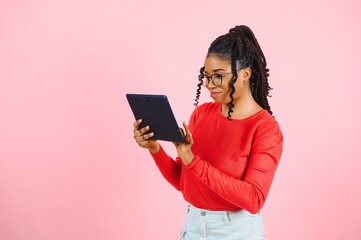 Young american student girl with curly african hair holding digital tablet and smiling standing over isolated pink background with copy space for text, logo or advertising.