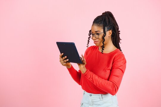 Young american student girl with curly african hair holding digital tablet and smiling standing over isolated pink background with copy space for text, logo or advertising.