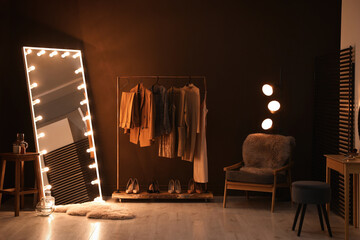 Stylish mirror with light bulbs and comfortable armchair in dressing room. Interior design