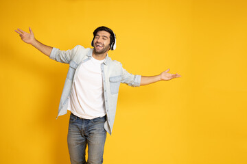 Naklejka premium Young man listening music with wireless headphones and dancing isolated on yellow background