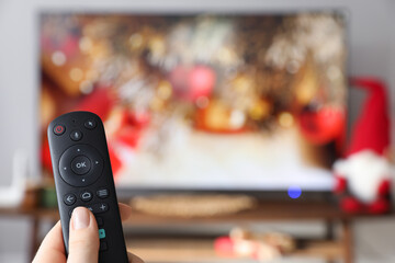 Woman with remote control watching TV at home, closeup. Space for text