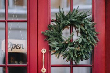 A spruce Christmas wreath hangs on the front red door of the store next to the 
