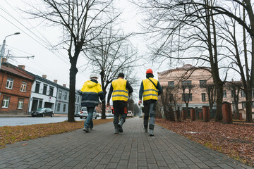 Three builders in yellow work uniforms and helmets walk down the street (1146)