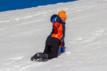 ni&ntilde;o saludando mientras juega en la nieve con gorro naranja