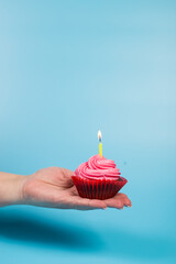 Bithday cupcake in female hand. Cupcake with candle on blue background. Lonely birthday.