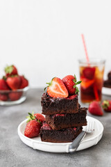 Pieces of fresh chocolate brownie with strawberries on a concrete background. Stack of fudgy chocolate brownies with strawberries on a concrete background. Homemade bakery and dessert.