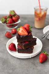 Pieces of fresh chocolate brownie with strawberries on a concrete background. Stack of fudgy chocolate brownies with strawberries on a concrete background. Homemade bakery and dessert.