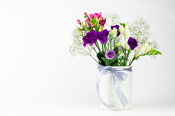 Different colors beautiful flowers bouquet in vintage white vase with ribbon on white background.
