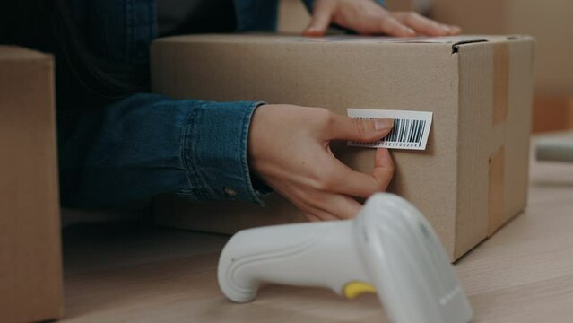 Cropped view of the asian woman putting sticker with barcode at the parcel while working at the home office. Post service and small business concept.
