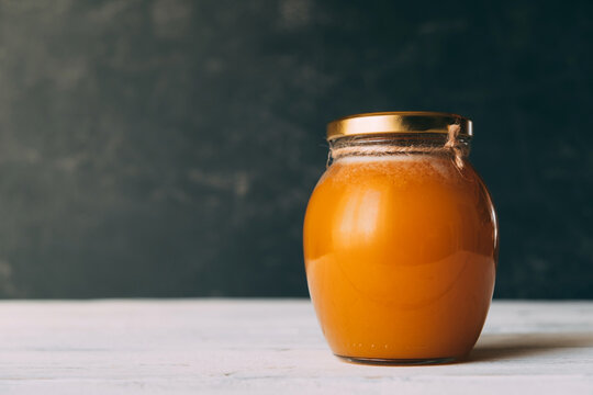 Glass jar with natural homemade honey on white table against dark background. Copy space.