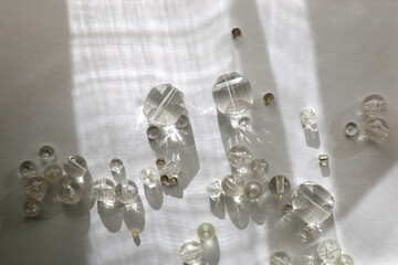 Various transparent beads on white background, illuminated by sunlight and reflectiing light. Flat lay.