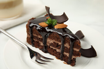 Piece of tasty homemade chocolate cake with mint and almonds on plate, closeup