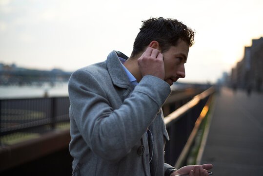 Business man at dawn in the city putting earbuds in his ear
