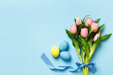 Easter eggs and a bouquet of pink tulips on a blue background. Top view flat lay copy space.