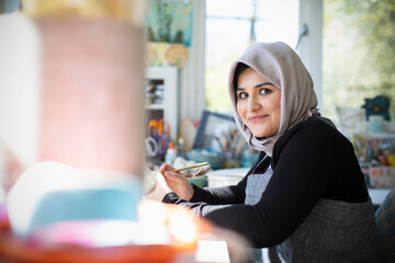 Portrait confident young female artist in hijab in art studio
