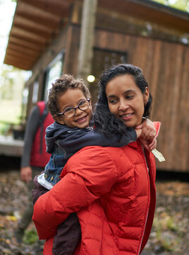 Portrait mother piggybacking cute son outside cabin