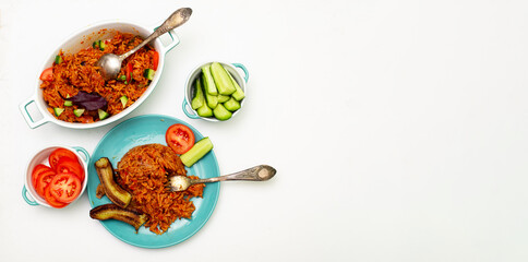 Jollof rice with fried banana on a plate. Rice with tomatoes, onions, spices. Fresh vegetables. White background. View from above. Banner. Place for text.