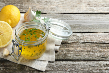 Jar with lemon sauce and ingredients on wooden table, space for text. Delicious salad dressing