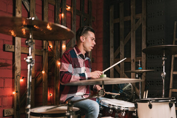 Serious man in casual wear playing drums and beating out rhythm in loft studio during music...