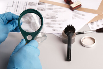 forensic expert using a magnifying glass examines fingerprints on evidence - a glass cup, forensic...
