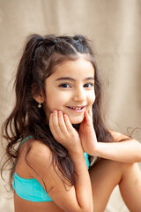 Funny little girl about 6 years old in a casual summer swimsuit posing on a plain beige background....