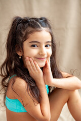 Funny little girl about 6 years old in a casual summer swimsuit posing on a plain beige background....